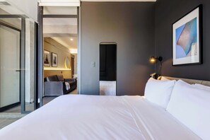 A hotel room with a large bed, a desk with a chair, a framed picture on the wall, and a door leading to another room. - w* | Nest-Style 1BR in Lively Tabacalera (Ciudad de México)