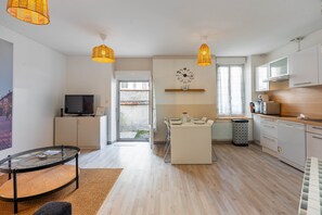 A modern kitchen with white cabinets, a dining area with a glass table, and a living room with a TV and wicker lamps. - L'agréable de Pierre - 900 m de la gare (Nancy)