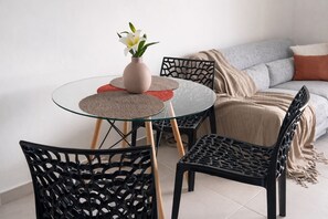 A modern living room with a glass table, black chairs, a beige sofa, and a decorative vase with a white flower. - Cosy apartment in the center of the island - View of the Mornes and the bay! (Fort-de-France)