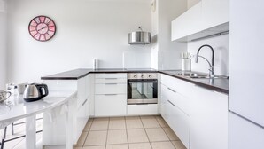 A modern kitchen with white cabinets, a stainless steel oven, a kettle, a sink, and a wall clock. - La Terrasse de La Ciotat - climatisé, proche plage (La Ciotat)