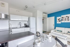 Une cuisine moderne avec des armoires blanches, une hotte en acier inoxydable et un coin repas comprenant une table et des chaises blanches.