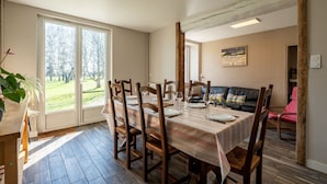 Ein Essbereich mit Tisch für vier Personen, Holzkästen, einer Couch und Blick durch eine Glastür.