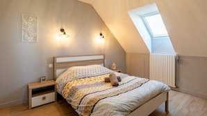 Ein Schlafzimmer mit schrägem Dach, einem Oberlicht, einem Bett mit gemusterten Betttextilien, Nachttischen und Wandleuchten.