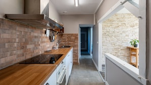 Eine schmale Küche mit Holzausziehtisch, Ziegelrückwand und einer Steinwand im Hintergrund.