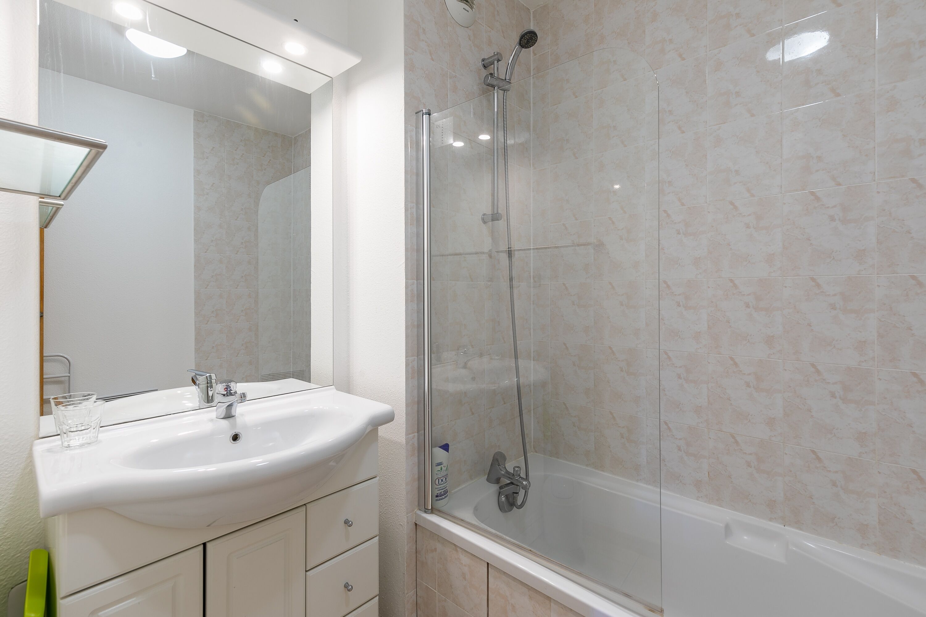 Un baño con ducha de vidrio, un lavabo blanco y un espejo sobre él.