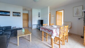 Un salon comprenant un canapé, une table basse, une table à manger avec des chaises, un téléviseur et une porte donnant sur une autre pièce.