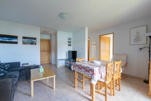 Un salon comprenant un canapé, une table basse, une table à manger avec des chaises, un téléviseur et une porte donnant sur une autre pièce.