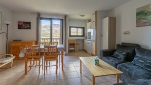 Un salon avec un canapé, une table à manger et des chaises, un coin cuisine et une vue sur les montagnes par les fenêtres.