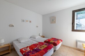 Une chambre avec deux lits, une table de chevet, une lampe et une fenêtre.
