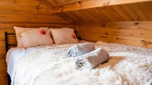 Una habitación de cabaña de madera con una cama, almohadas y una toalla enrollada.