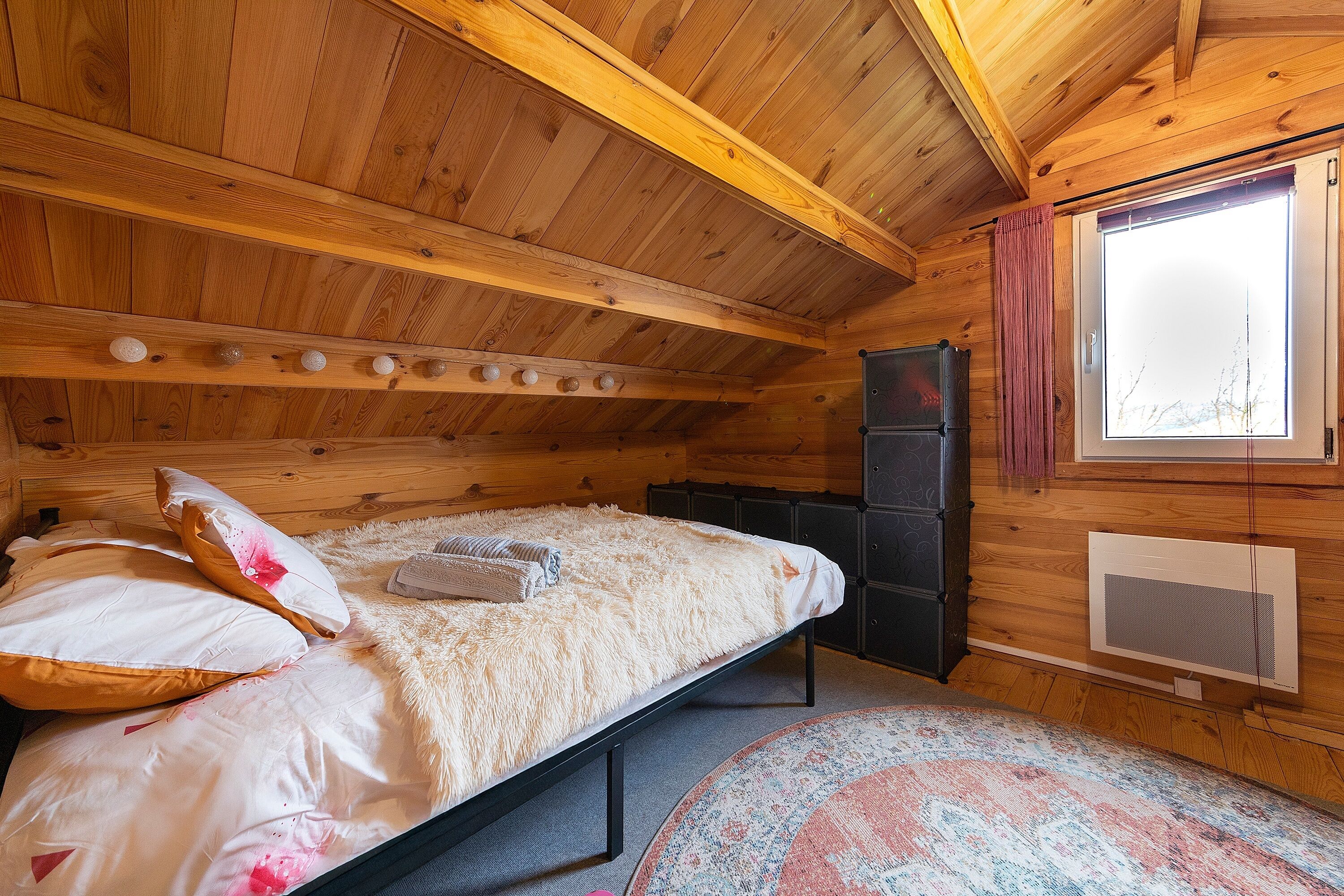 Un dormitorio de cabaña de madera con cama, almohadas, un calentador y una ventana.