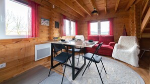 Interior de una cabaña de madera con una mesa de comedor, sillas, un sofá rojo y una silla blanca.