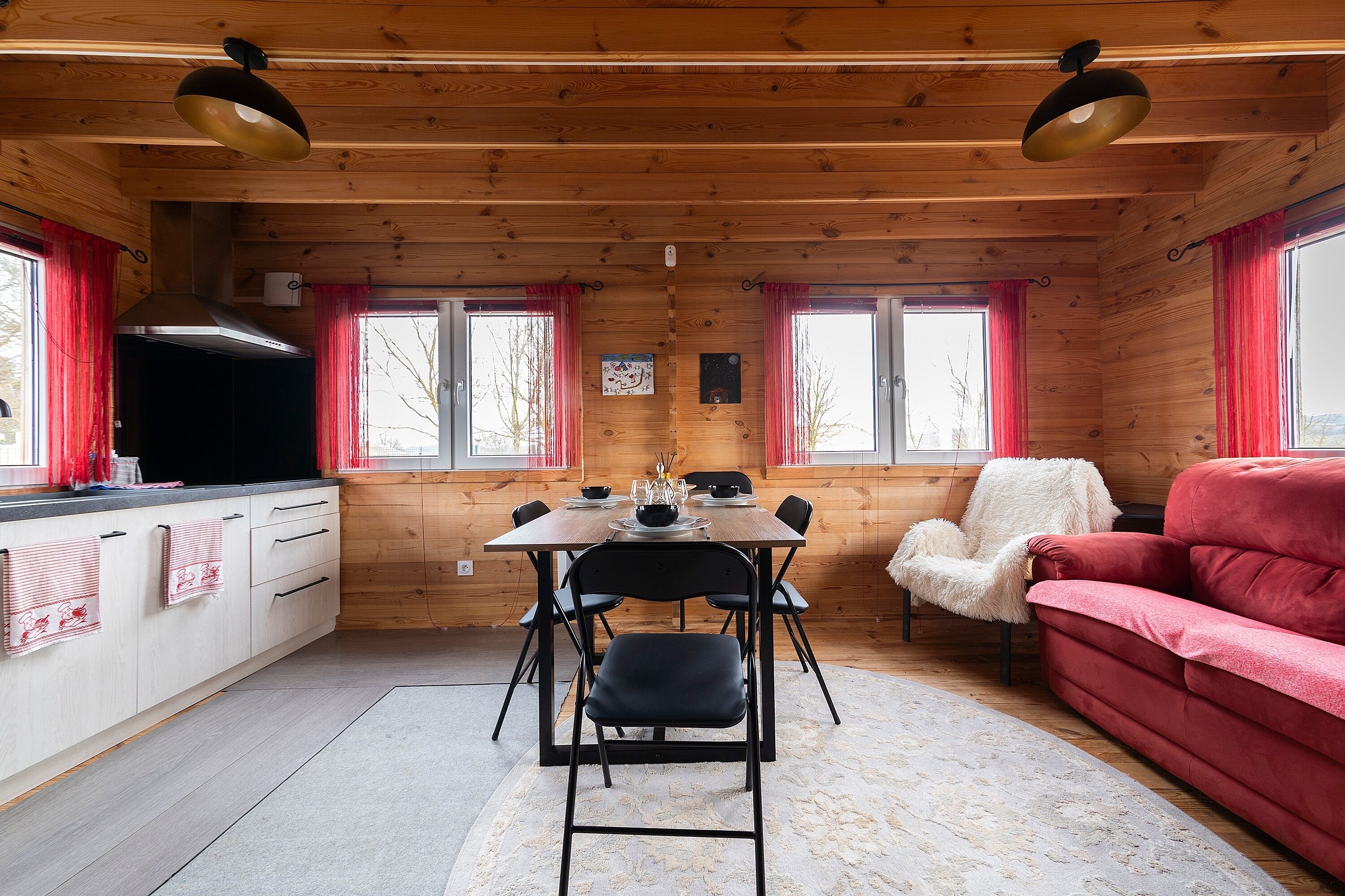 Interior de una cabaña de madera con una mesa de comedor, sillas, un sofá y un televisor.