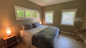 Une chambre à coucher avec un lit, une lampe de chevet, des stores aux fenêtres et un étendoir à linge.