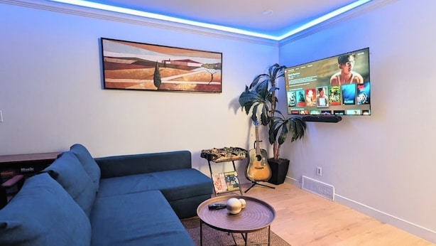 A living room with a sectional sofa, a flat-screen TV, a plant, and a small table with a remote control.