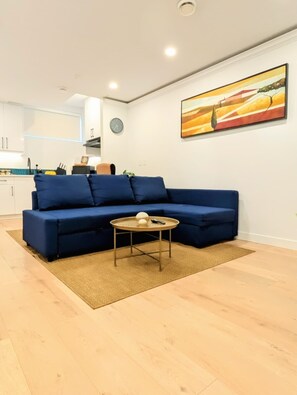 A living room with a blue sofa, a round coffee table, and a painting on the wall. - Sanctum - Luxury and Modern Gateway Suite (Calgary)