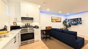 A modern kitchen with stainless steel appliances, a dining area with a blue sofa, and a flat-screen TV mounted on the wall.