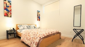 A bedroom with a wooden bed, a nightstand, a bedside table, a mirror, and two wall-mounted paintings.