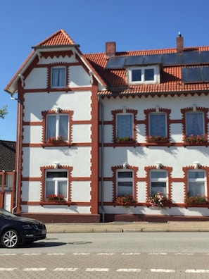 Ein zweigeschossiges Gebäude im traditionellen Baustil, mit rotem Ziegeldach und weißen Wänden mit braunen Verzierungen.