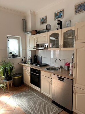 Eine Küche mit weißen Schränken, einer Edelstahl-Spüle, einem Geschirrspüler von Bosch und einem Fenster mit Jalousien.