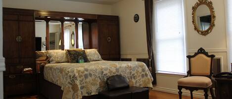 A bedroom with a large bed, a dresser, a chair, and a window with curtains.