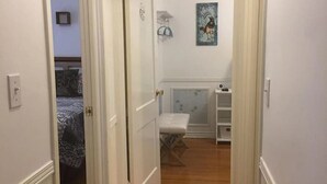 A narrow hallway with wooden flooring, white walls, and a door leading to a bedroom with a bed and a nightstand. - Cozy House located close Skylon Towery, Falls view Casino & Horseshoe Falls (Niagara Falls)