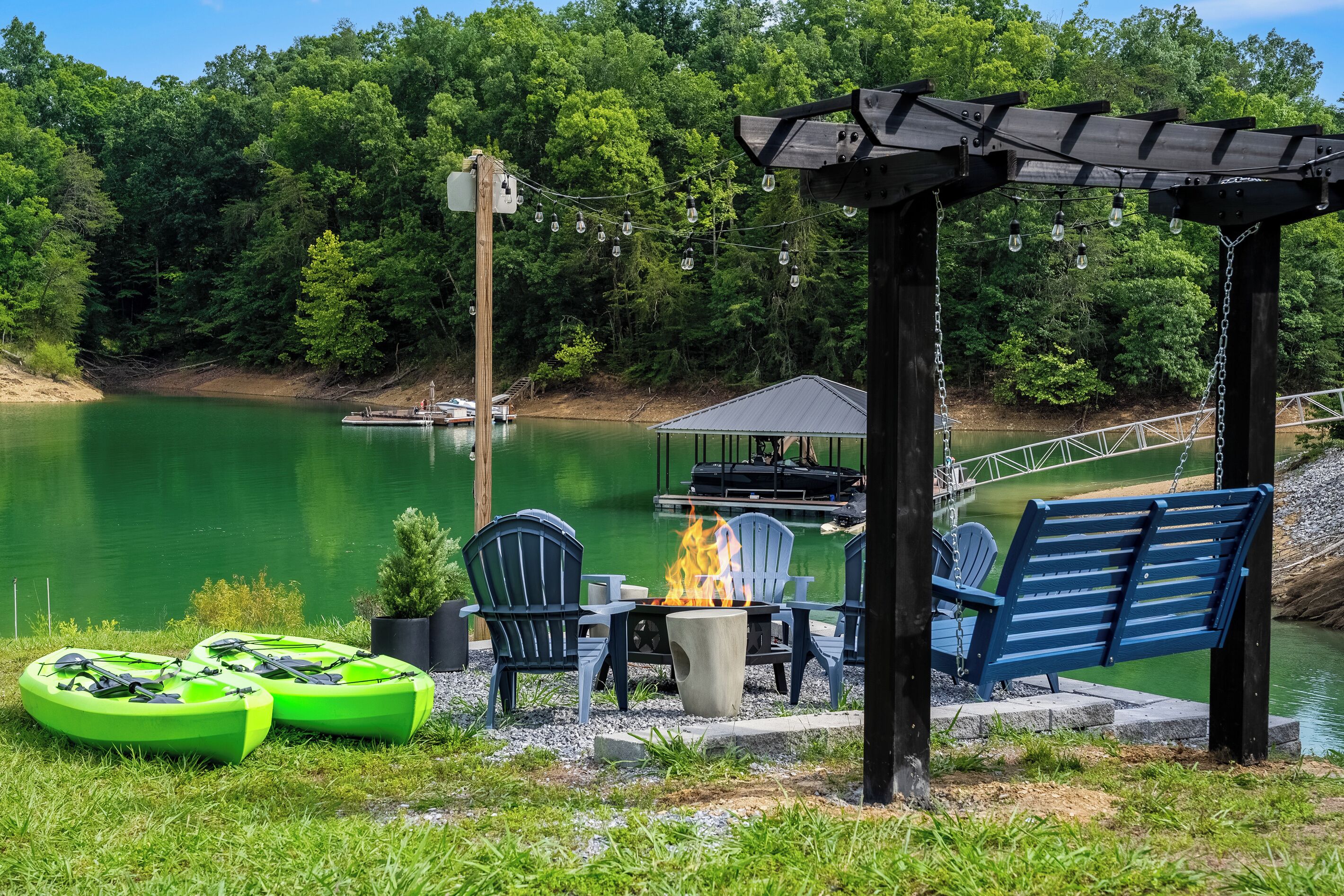 A lakeside patio with chairs, a fire pit, and kayaks.