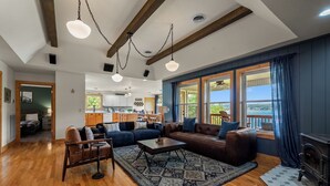 A spacious living room with a fireplace, a kitchen in the background, and large windows with curtains. - Brand New Lakefront Oasis: Private Dock & boat launch, Kayaks, Hot Tub (Sevierville)