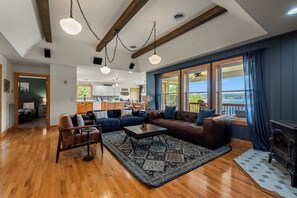A spacious living room with a fireplace, a kitchen in the background, and large windows with curtains. - Brand New Lakefront Oasis: Private Dock & boat launch, Kayaks, Hot Tub (Sevierville)