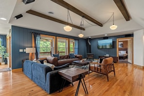 A spacious living room with a large sofa, a coffee table, and a fireplace. There are large windows and a television mounted on the wall. - Brand New Lakefront Oasis: Private Dock & boat launch, Kayaks, Hot Tub (Sevierville)