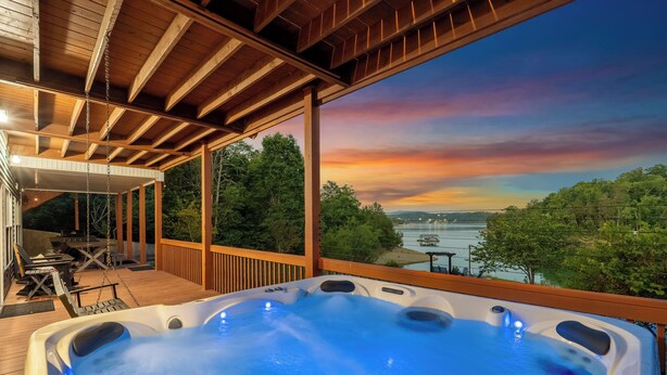 A hot tub on a wooden deck with a view of a body of water and trees. - Brand New Lakefront Oasis: Private Dock & boat launch, Kayaks, Hot Tub (Sevierville)