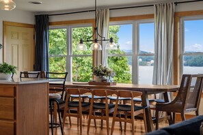 A dining area with a wooden table, chairs, and a view of greenery through large windows. - Brand New Lakefront Oasis: Private Dock & boat launch, Kayaks, Hot Tub (Sevierville)