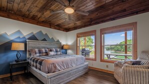 A bedroom with a bed, a chair, a ceiling fan, and a view of the outdoors. - Brand New Lakefront Oasis: Private Dock & boat launch, Kayaks, Hot Tub (Sevierville)