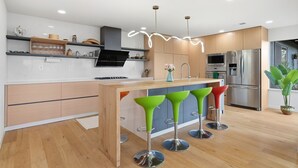 Une cuisine moderne avec des meubles en bois, un îlot central et des tabourets de bar aux couleurs vives.