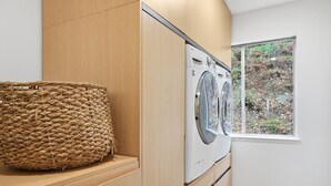 Une buanderie équipée d’un lave-linge, de meubles en bois et d’un grand panier en osier.