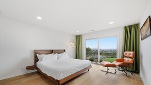 Une chambre à coucher avec un lit en bois, une chaise verte et une grande fenêtre donnant sur un beau paysage.