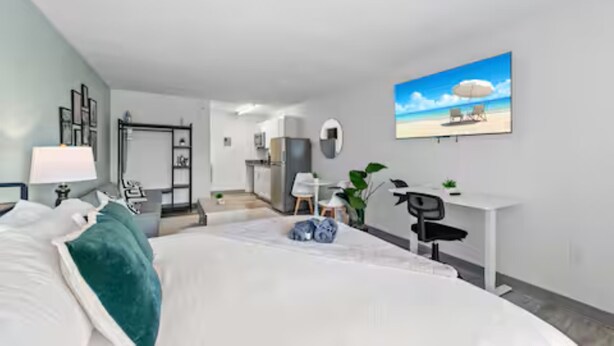 Une chambre d’hôtel moderne équipée d’un lit, d’un bureau, d’une chaise et d’un tableau représentant une scène de plage.