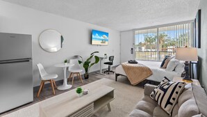 Une chambre d’hôtel moderne dotée d’une kitchenette, d’un coin repas, d’un canapé et d’une grande fenêtre offrant une vue sur les palmiers.