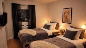 Camera d'albergo con due letti, televisore, un quadro appeso e una finestra con tende.