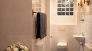Un bagno stretto con il water, un lavandino e un piccolo tavolino con un vaso di fiori.