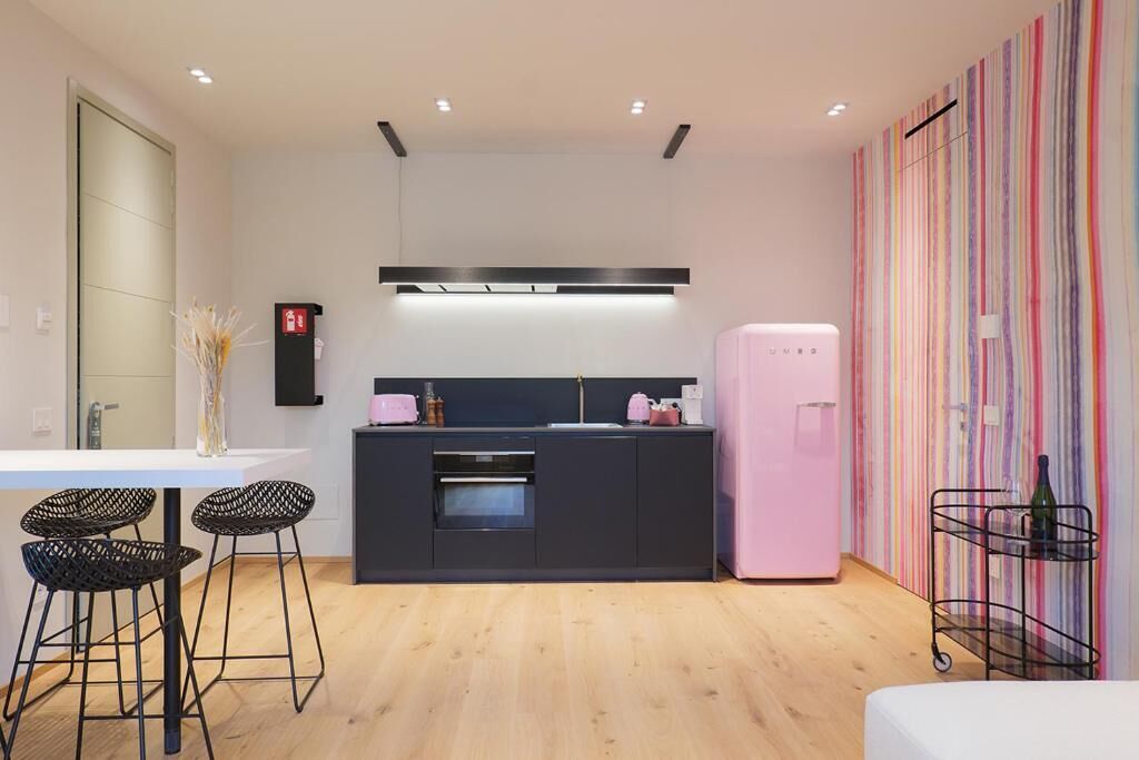 A modern kitchen with a central island, bar stools, a refrigerator, and a wall-mounted light fixture.