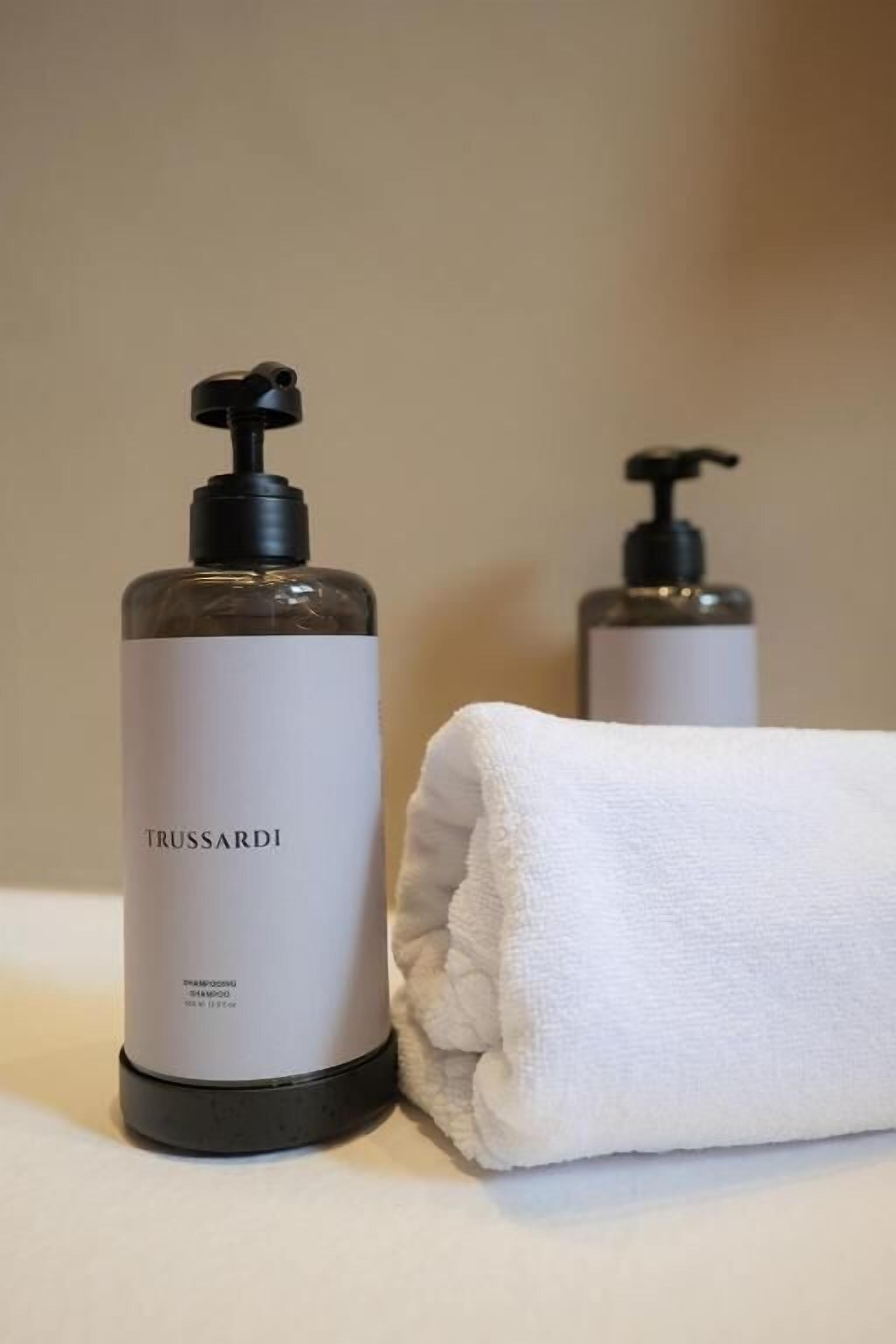 Zwei Flaschen Trussardi Shampoo und Conditioner sowie ein gefaltetes weißes Handtuch auf einer Oberfläche.