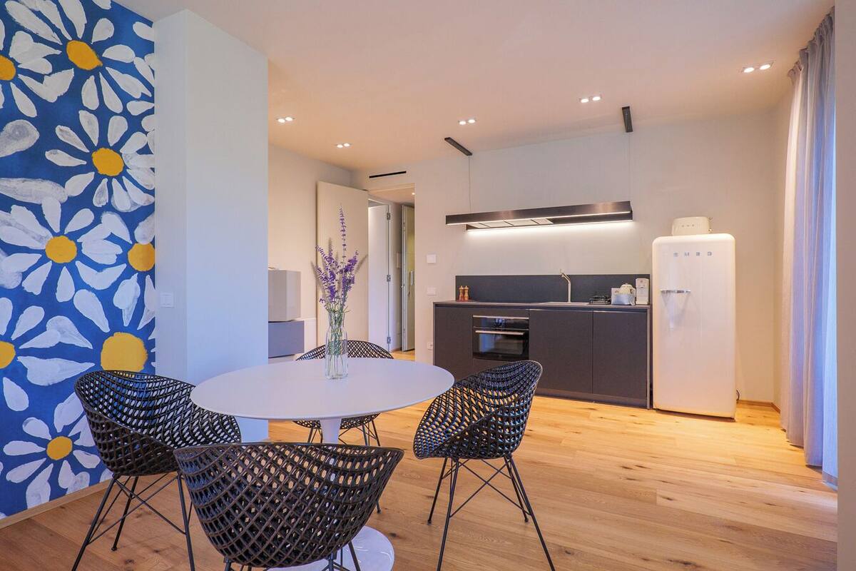 A modern kitchen with a refrigerator, oven, and sink. There is a dining area with a round table and four chairs.