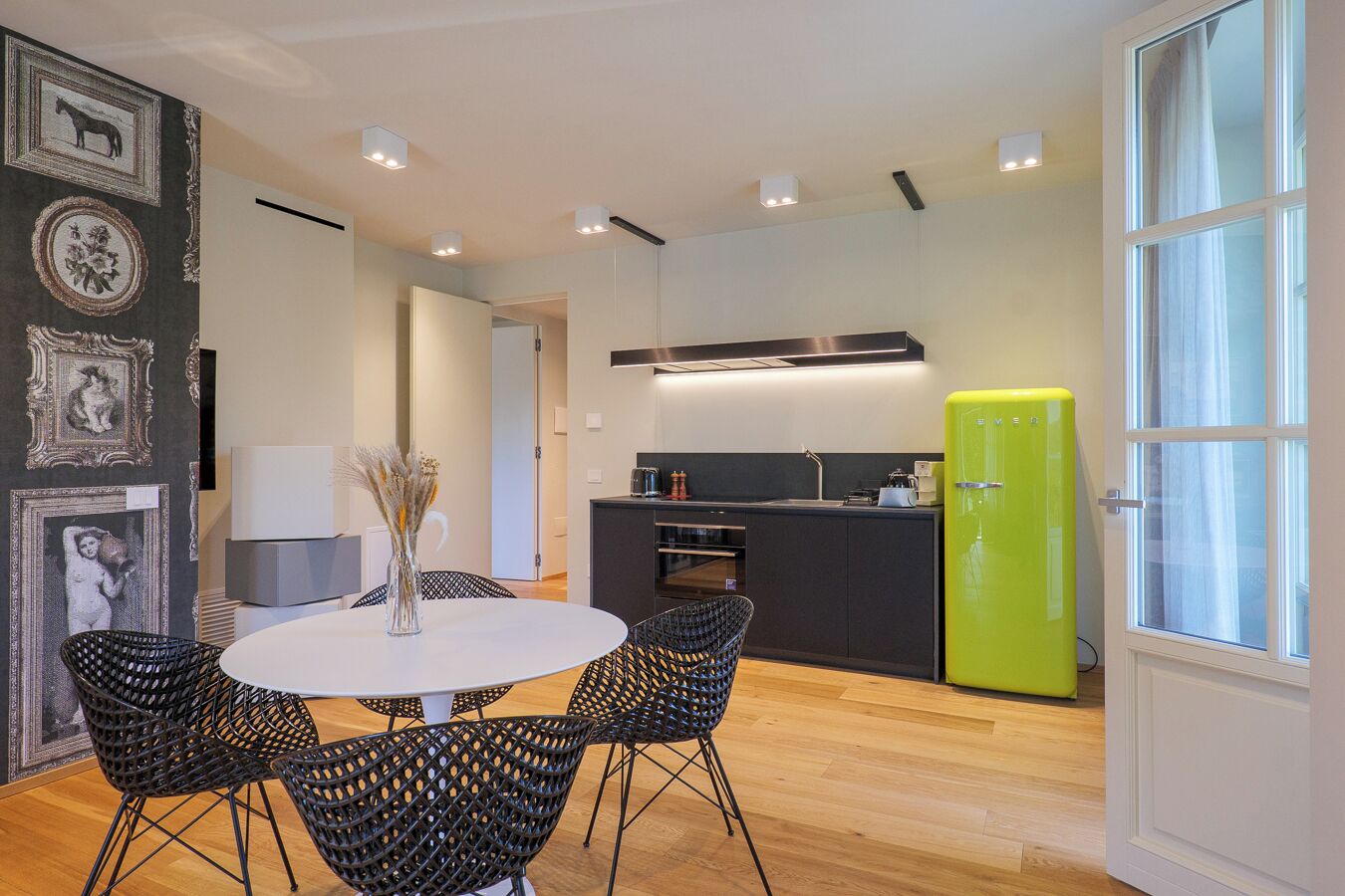 Una cocina moderna con un refrigerador verde, un área de comedor con una mesa redonda y sillas, y un pasillo con cuadros enmarcados.