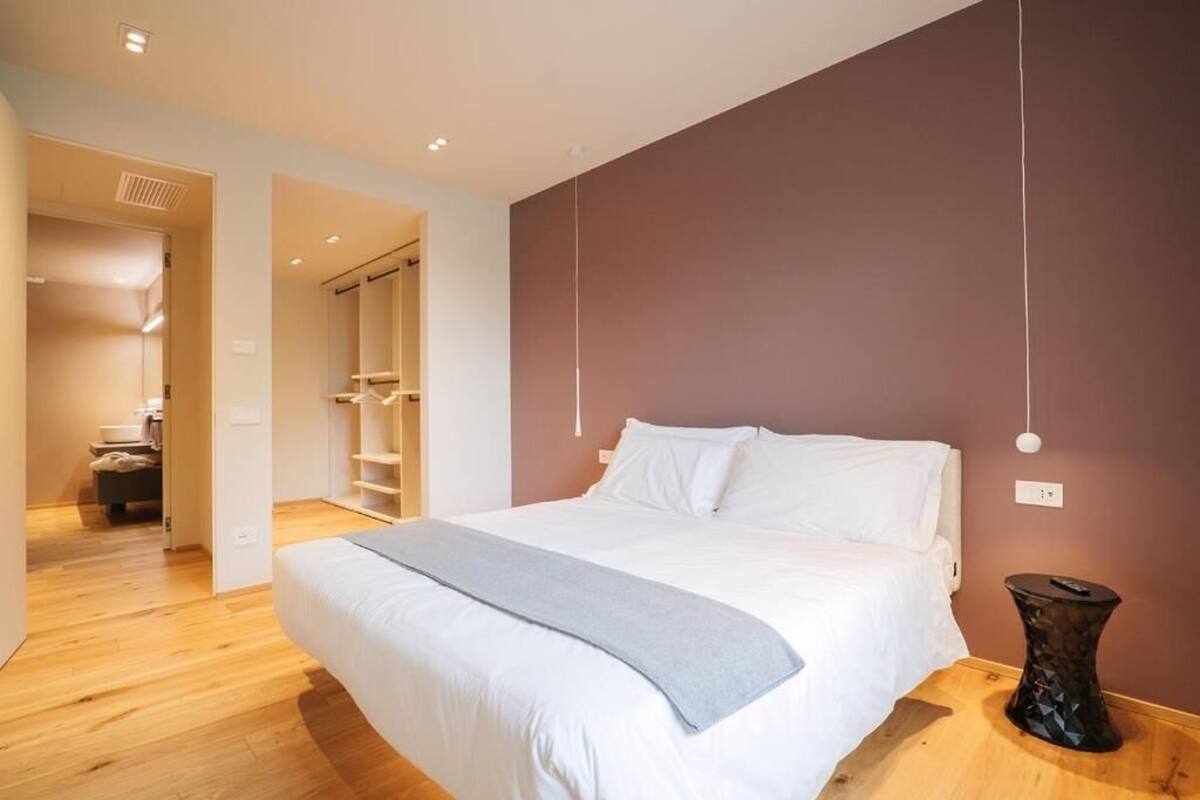 A modern bedroom with a large bed, wooden flooring, a wardrobe, and a small table.