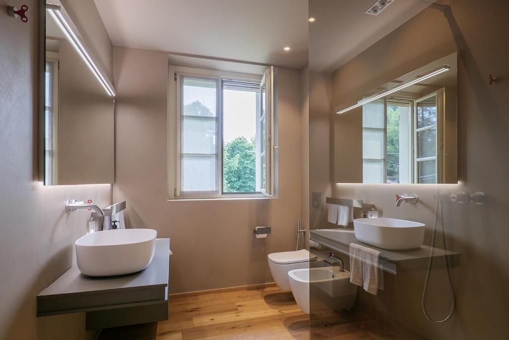 A modern bathroom with a large window, a sink, a toilet, and a shower.