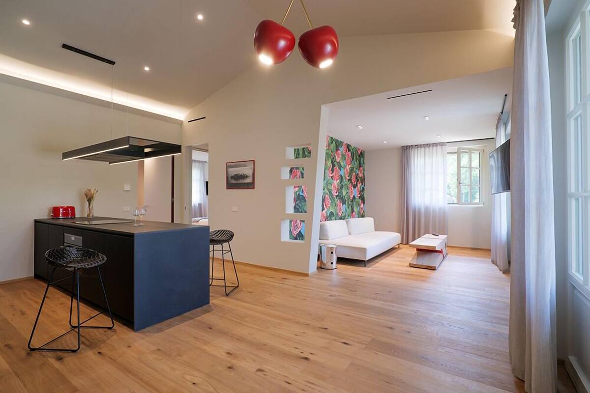 A modern kitchen with a central island, a dining area with a white sofa, and a living room with a large window.