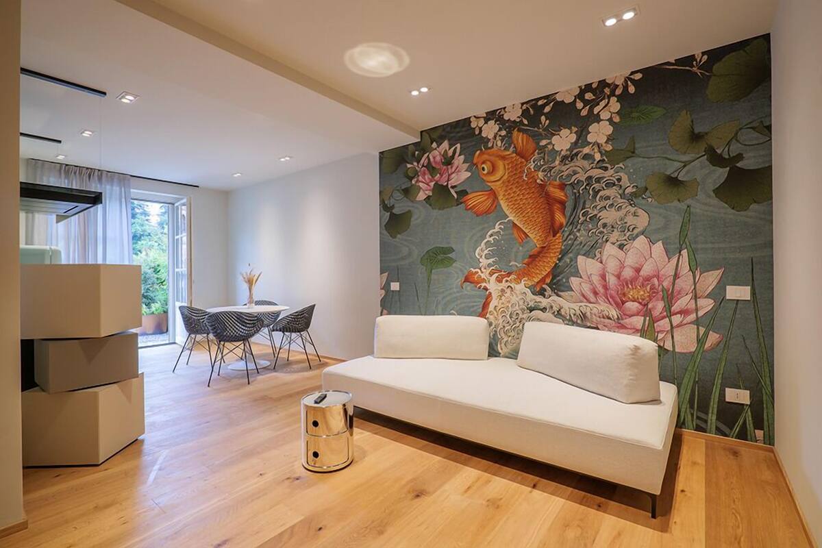 A modern living room with a white sofa, a dining table with chairs, a large fish mural on the wall, and a wooden floor.