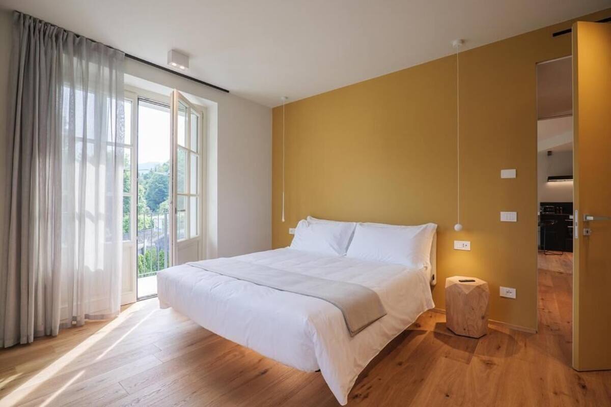 A bedroom with a large bed, a sliding door to a balcony, and a wooden floor.
