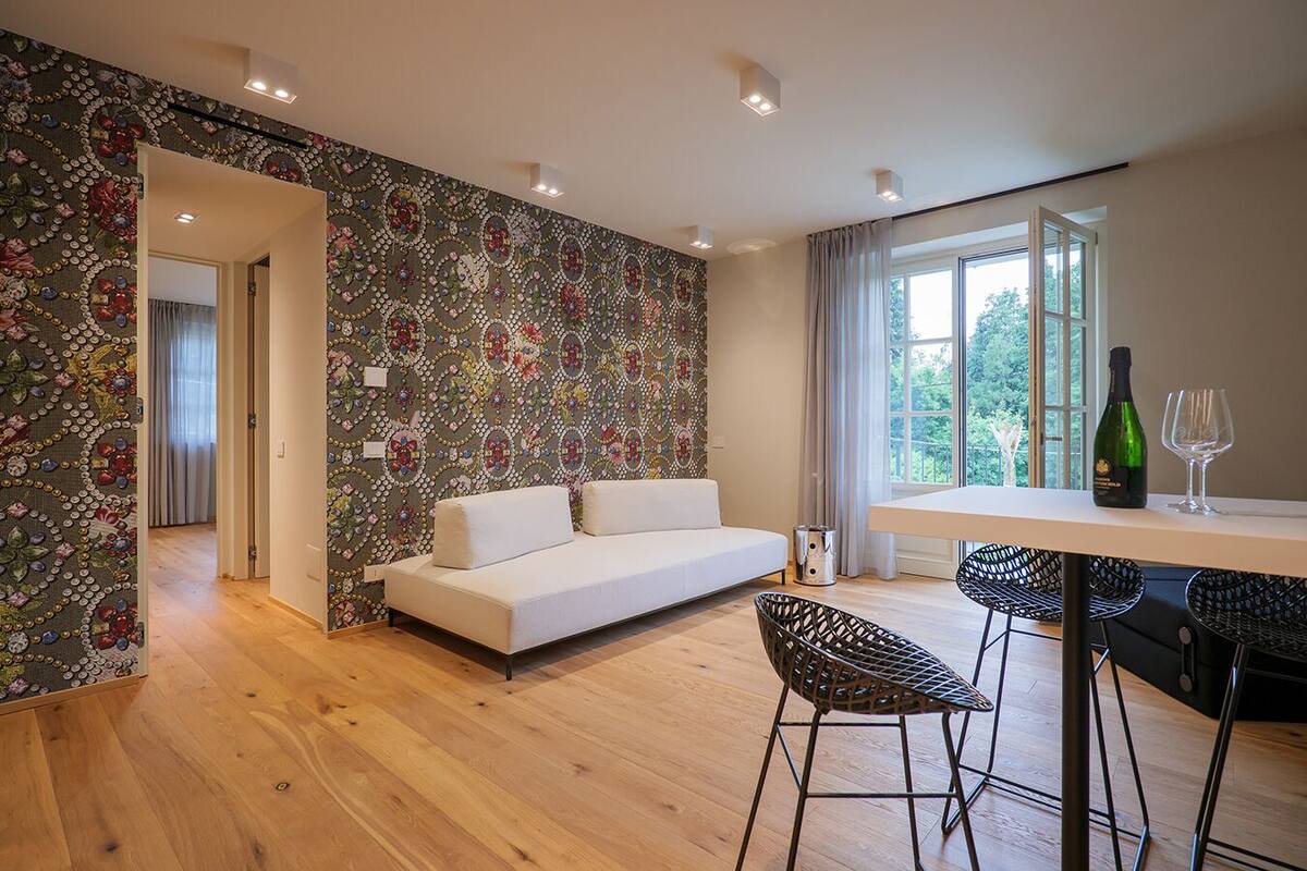 A modern living room with a white sofa, a dining table with chairs, and a patterned wallpaper.
